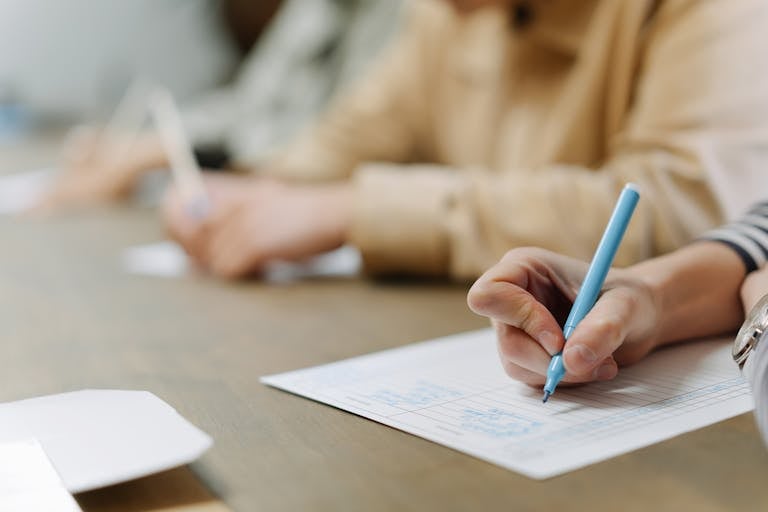 Focused hands writing on lined paper in a classroom setting, close-up view.